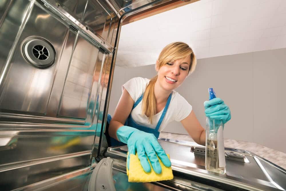 Woman cleaning the inside of a dishwasher with a spray bottle