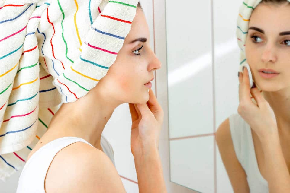 Young woman touching her cheek in the bathroom mirrorrr