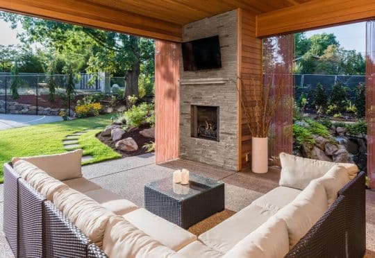 Outdoor living space with sectional couch, fireplace and outdoor tv mounted on a side wall