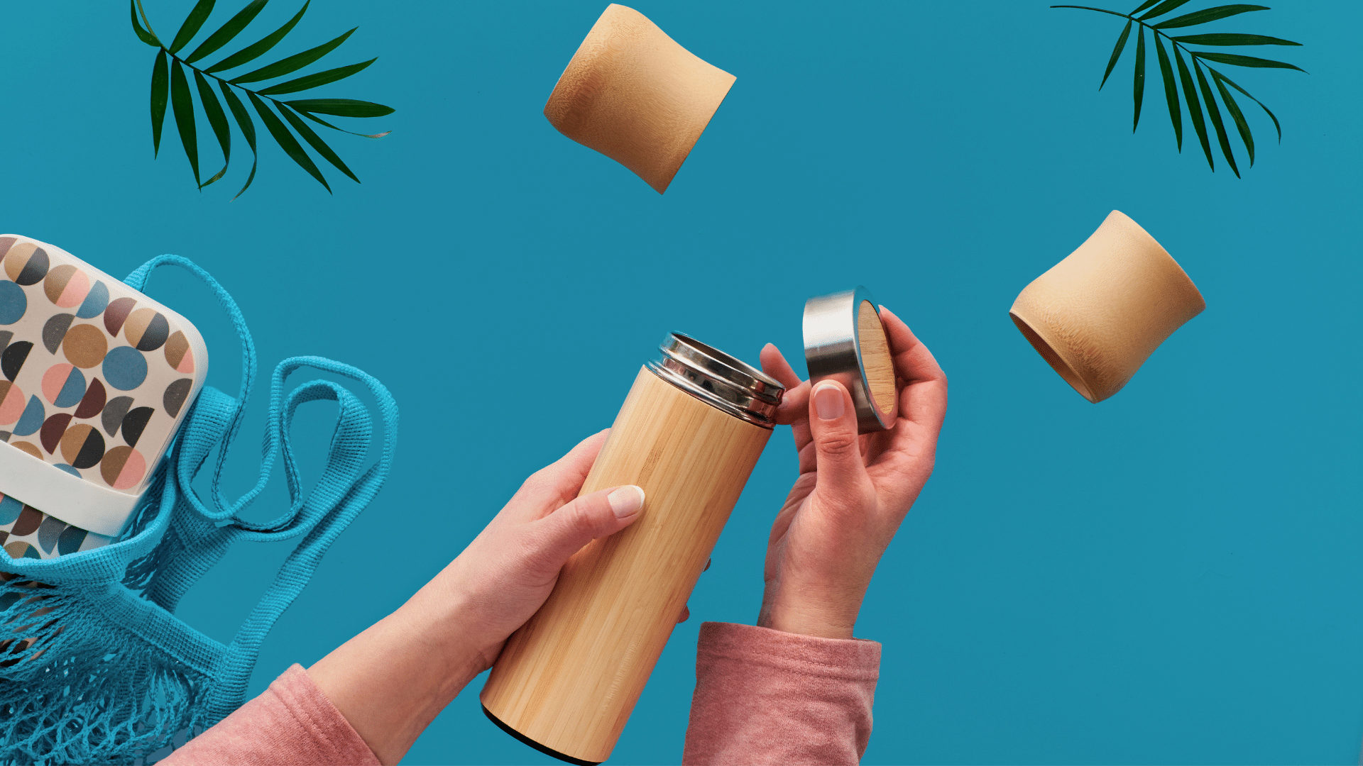 Hand holding and opening a bamboo water bottle over a solid turquoise background