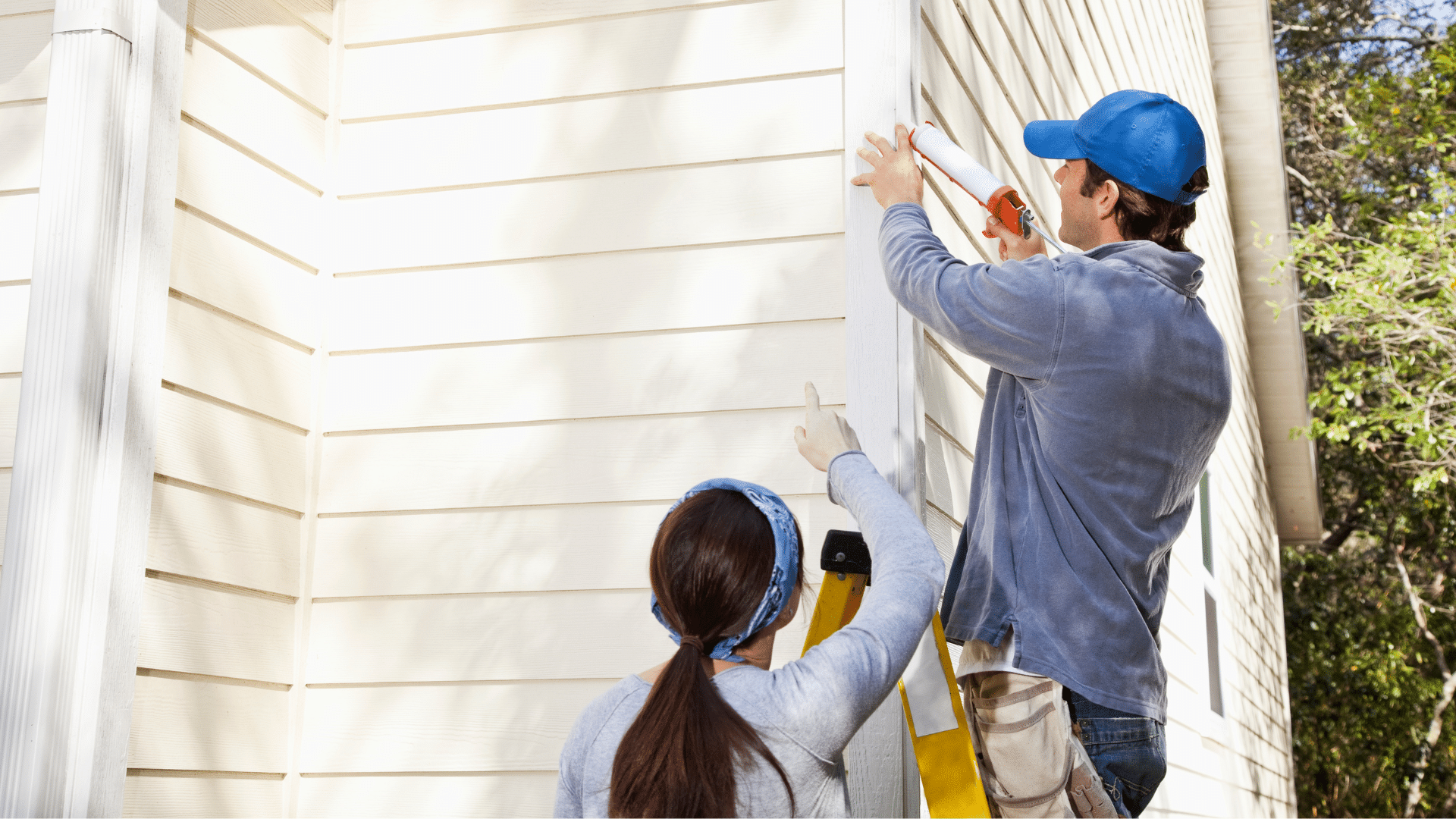 Couple fixing siding on their house with a ladder