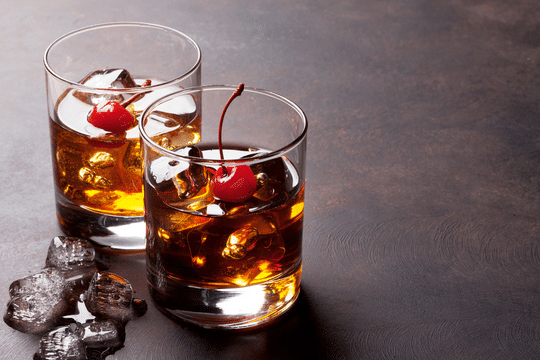 Two glasses filled with Manhattan cocktails and topped with maraschino cherries