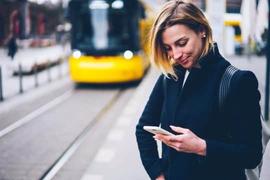 Woman looking at her phone while a city bus approaches in the background