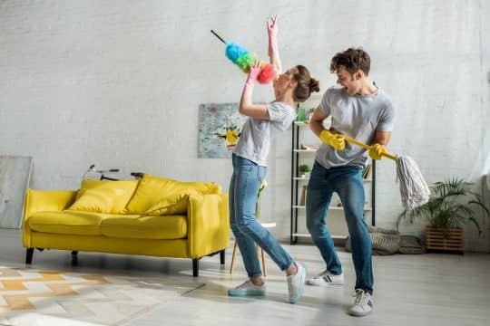 man and woman with household singing while doing spring cleaning in living room