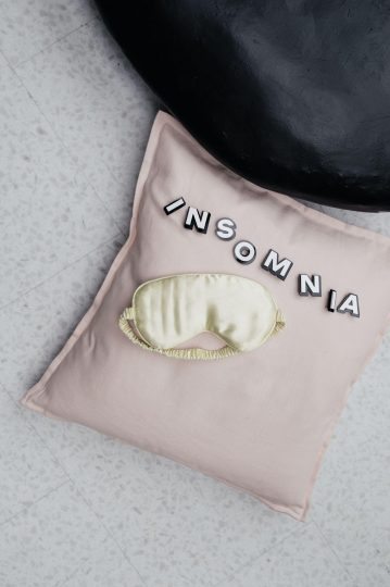 Pink pillowcase with the word insomnia spelled out. A cream silk eyemask is on top. 