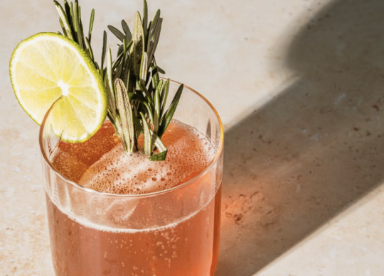 Pink cocktail with lime slice and rosemary sprigs